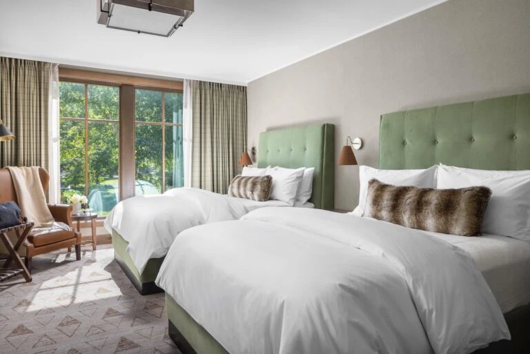 Two queen beds with green headboards in a bright hotel room.