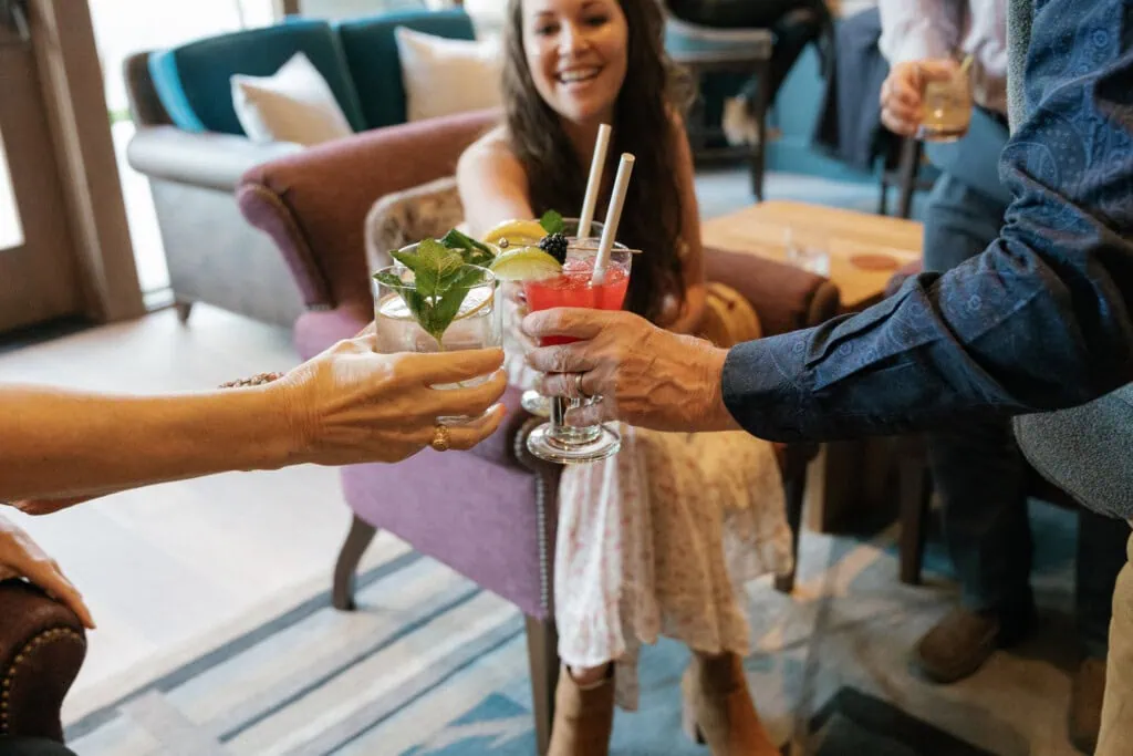 Group of people clinking colorful cocktails in a cozy lounge setting.