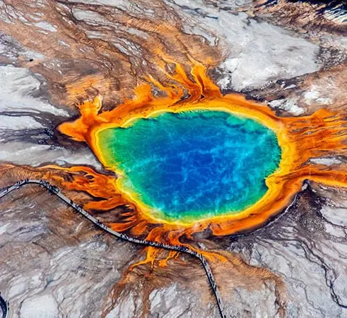 Hot spring with vibrant blue water surrounded by orange and brown mineral deposits.