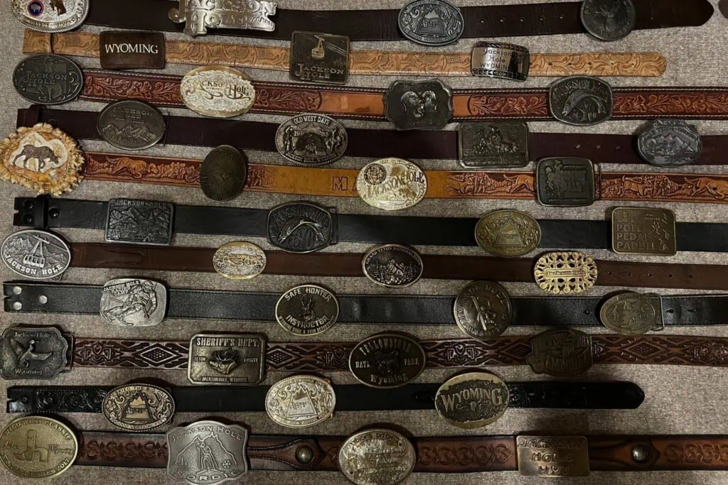 Vintage belt buckles collection displayed on wooden slats. The buckles vary in shape, size, and desi.