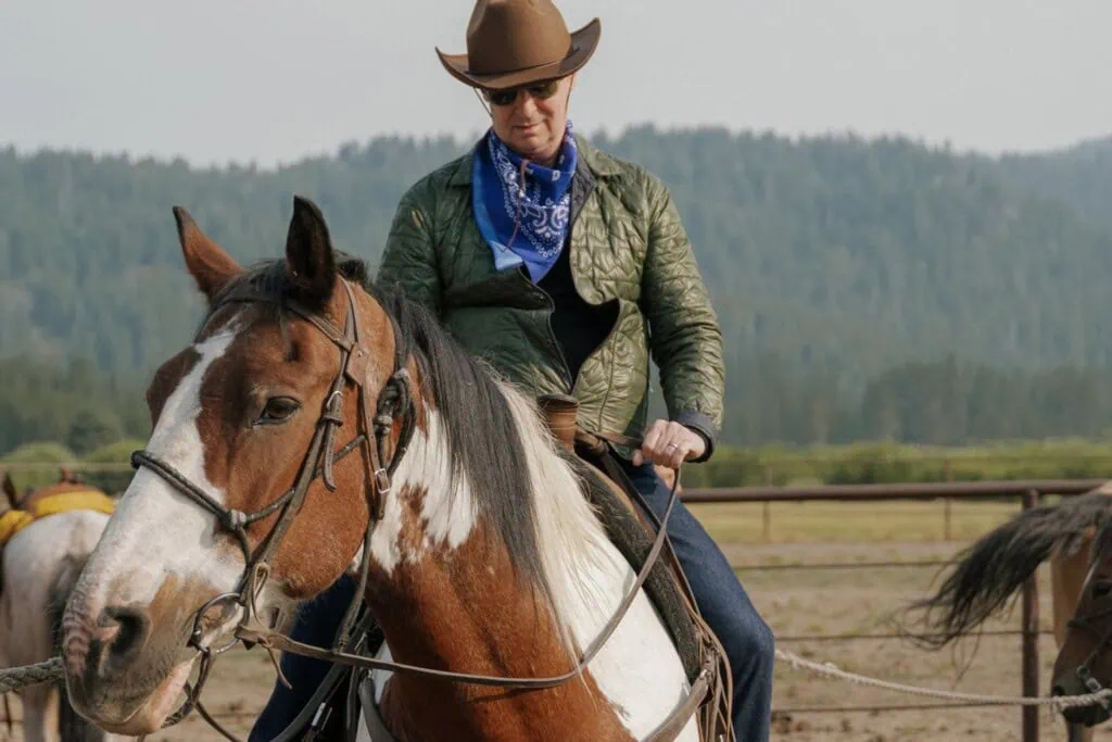 Rider wearing a cowboy hat and sunglasses on a brown and white horse outdoors.