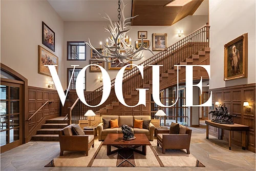 Vogue logo over a luxurious living room with wooden staircase and chandelier.