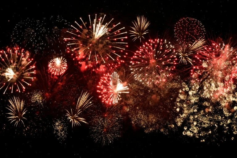 Fireworks exploding in the night sky with red, gold, and white colors.