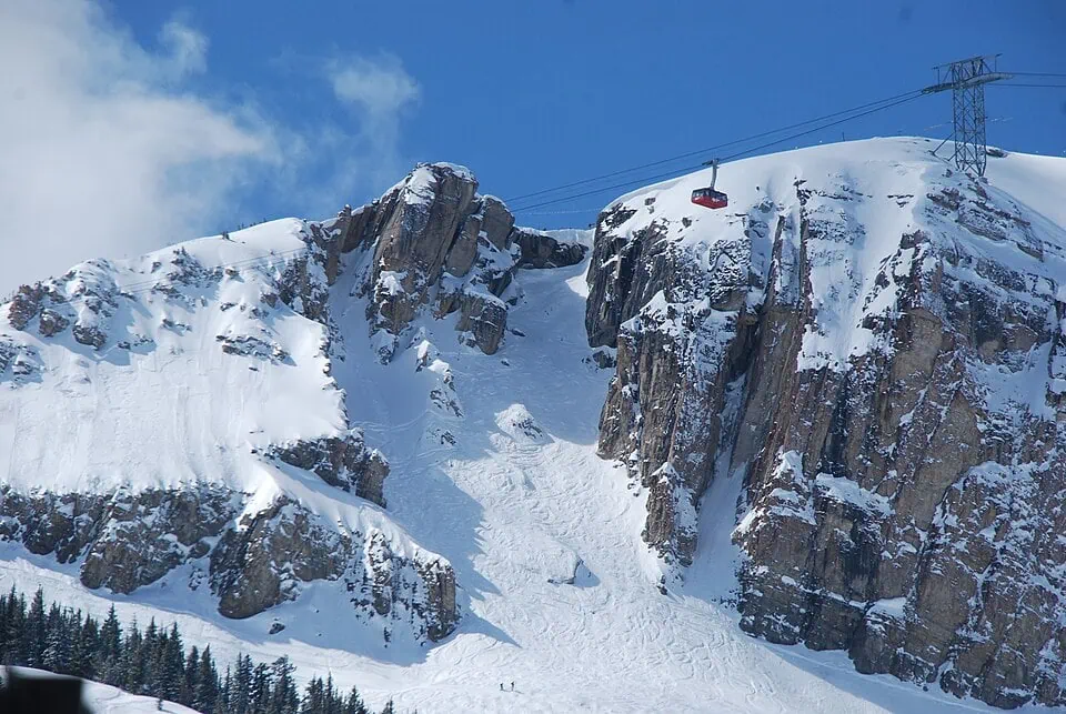 Snow-covered mountain with a ski lift and rocky cliffs under a blue sky.