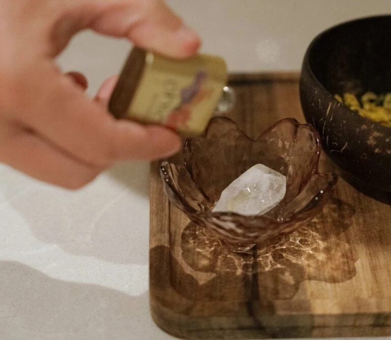 Hand holding a matchstick over a glass bowl with a large white crystal inside.