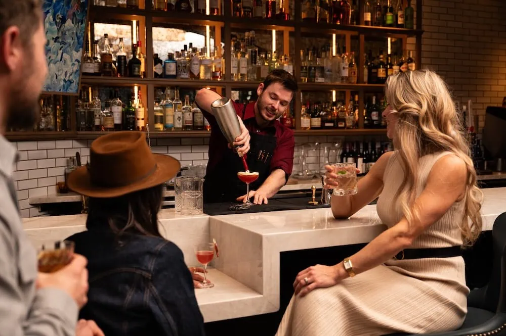 Bartender pouring a cocktail for a woman at the bar.