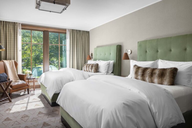 Two double beds with green headboards in a bright hotel room.