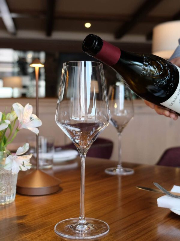 Person pouring red wine into a glass at a restaurant table.