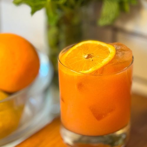 Orange cocktail with a slice of orange on top, in a glass with ice.