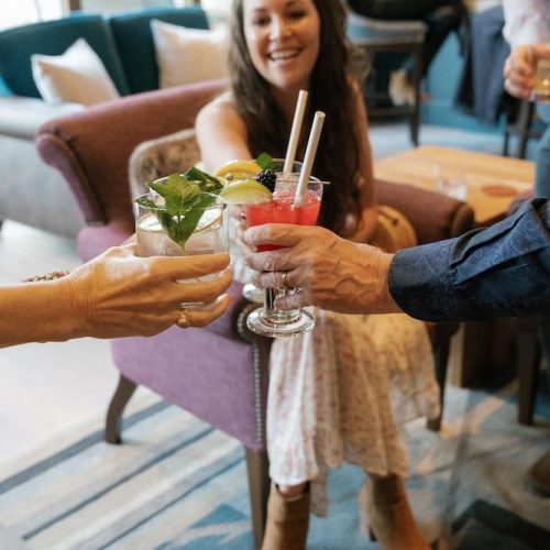 People clinking colorful cocktails at The Wild Sage Bar.