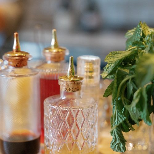 Assorted bottles of bitters and a bunch of fresh herbs on a tray.