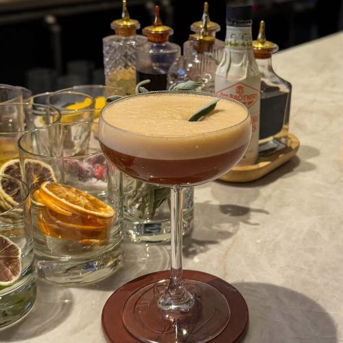 Cocktail with frothy top and lime garnish on a bar counter.