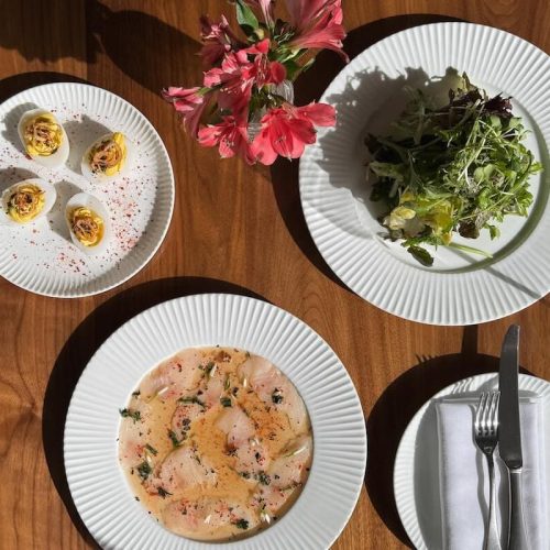 Salad, soup, and appetizers on white plates with pink flowers on wooden table.