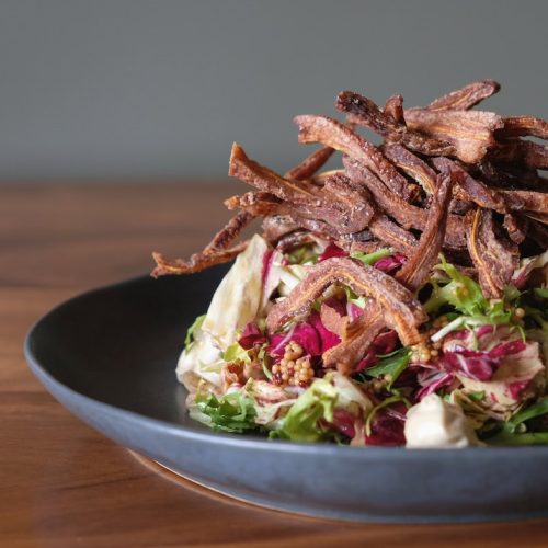 Salad with shredded beef on top in a black bowl on a wooden table.