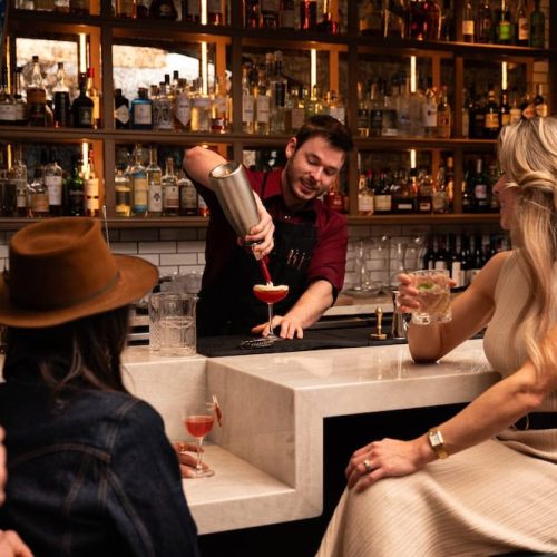 Bartender pouring a cocktail for a woman at the bar.