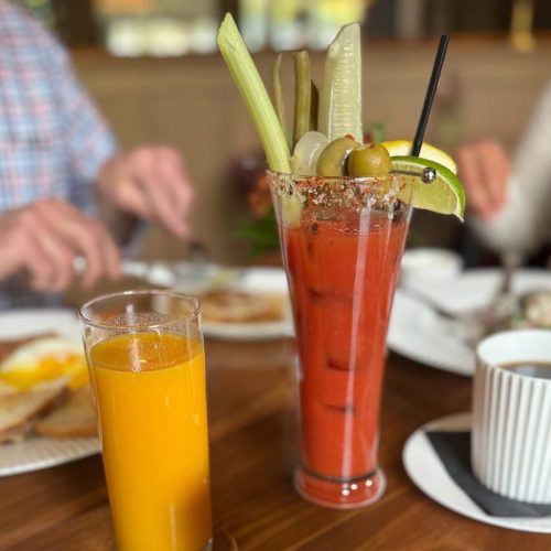 A tall glass of Bloody Mary with celery, olives, lime, and a straw.