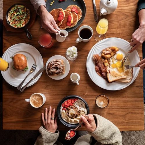 People enjoying breakfast with various dishes and drinks on a wooden table.