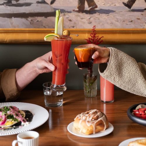 Two people clinking colorful cocktails at a restaurant table.