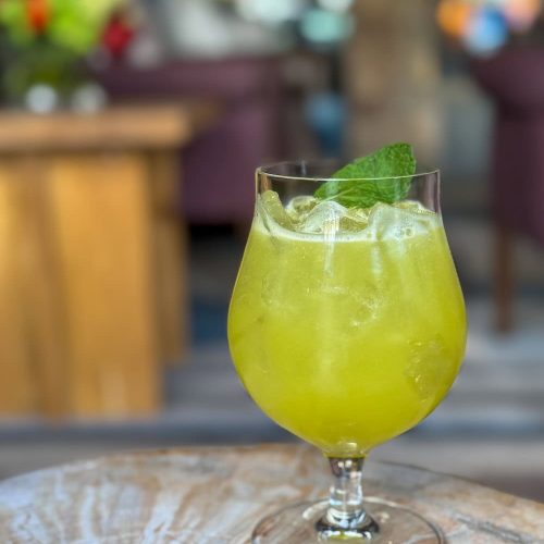 Green cocktail with mint leaf in a glass on a wooden table.