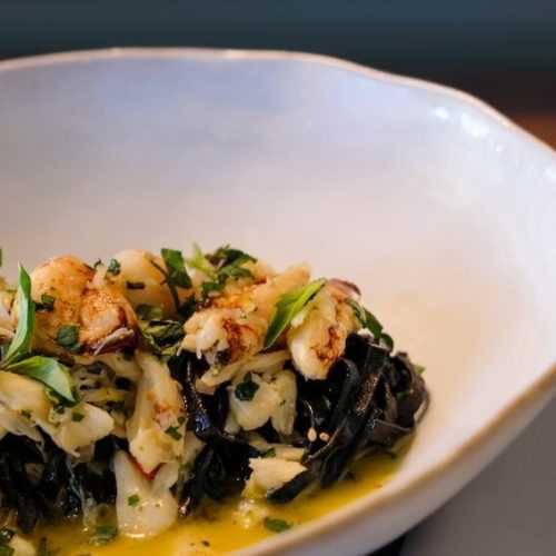 Seafood pasta with green herbs in a white bowl on a wooden table.