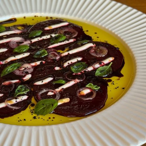 Beet carpaccio with basil, olive oil, and balsamic vinegar on a white plate.