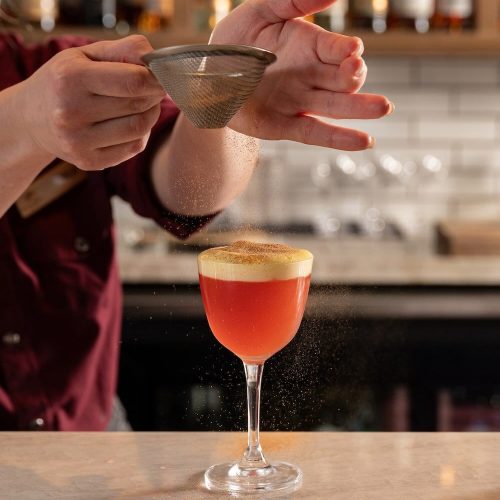 Bartender sifts cocktail ingredients into a glass at The Wild Sage Bar.
