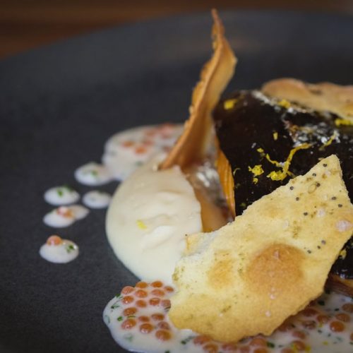 Gourmet dish with fish, sauce, and garnishes on a black plate.