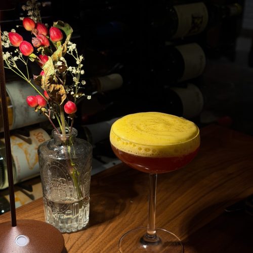 Colorful cocktail with yellow foam on top on a wooden bar counter.