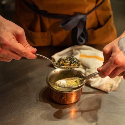 Person in apron serving spinach dish with a spoon and ladle.
