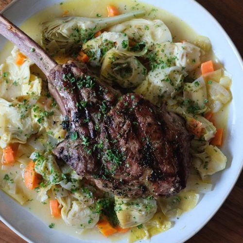 Lamb chop with vegetables and herbs on a white plate.