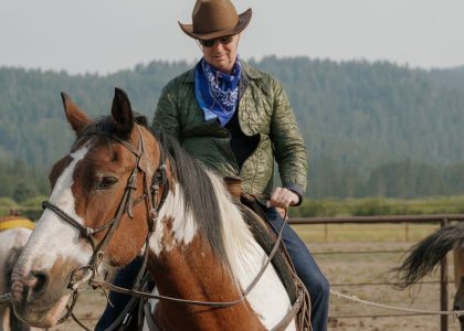 Rider wearing a cowboy hat and sunglasses on a brown and white horse outdoors.