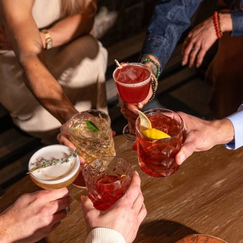 People clinking colorful cocktails in a bar setting.