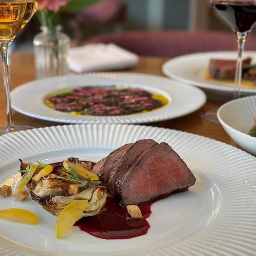 Elegant dinner table with a plate of sliced beef, wine glasses, and other dishes.