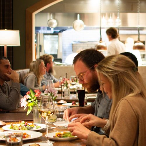 People dining at a restaurant with a view of the kitchen in the background.