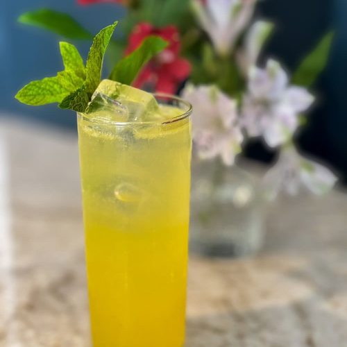 Tall yellow cocktail with mint and lime on a marble table.