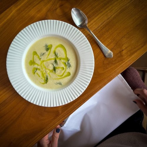 Bowl of creamy soup garnished with lemon slices and herbs on a wooden table.
