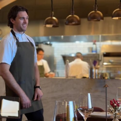 Smiling waiter in apron serving customers in a restaurant.