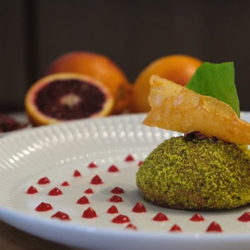 Fried green ball with a leaf and crispy topping on a white plate.