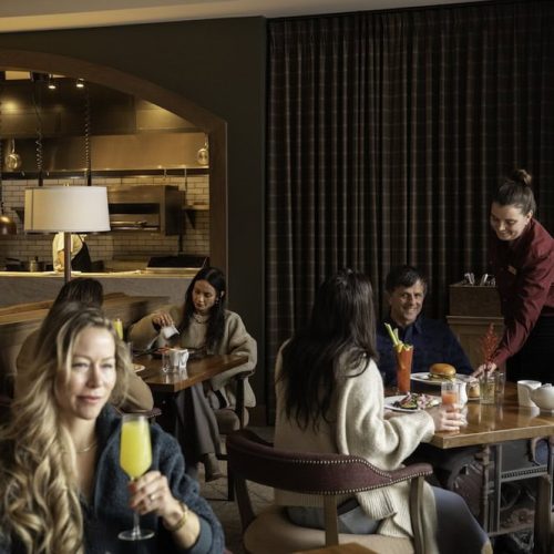 Group of people dining in a restaurant with a waitress serving drinks.