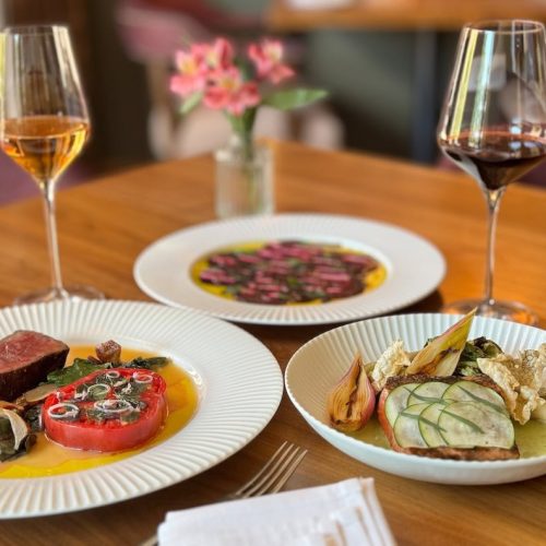 Elegant dinner table with wine glasses, a meat dish, and a vegetable dish.