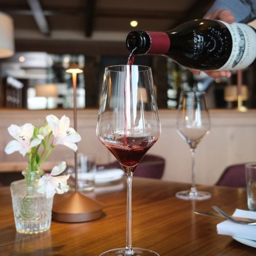 Person pouring red wine into a glass at a restaurant table.