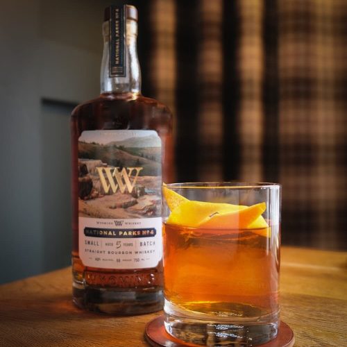 Bottle of whiskey and a glass with an amber drink and lemon slice.